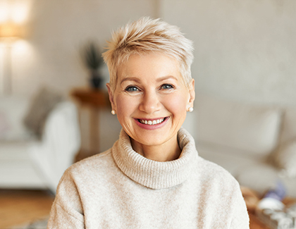 A smiling woman in a sweater sitting in a living room.
