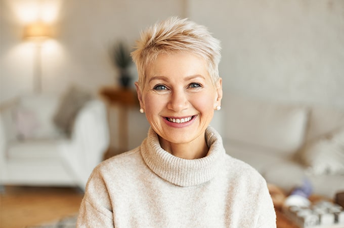 A smiling woman in a sweater sitting in a living room.